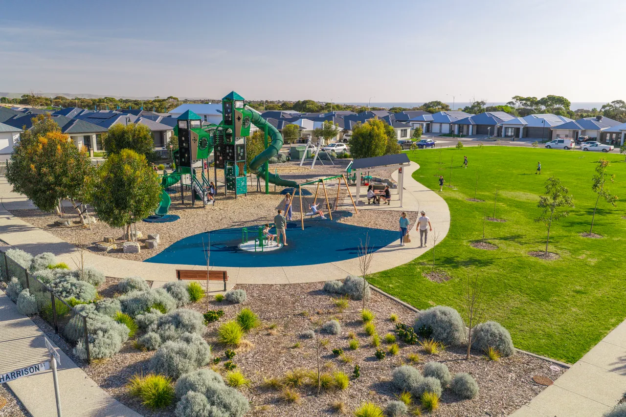An aerial view of a playground, parkland and new homes in late afternoon light