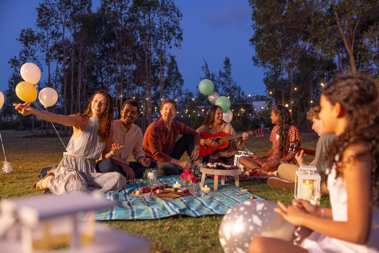 Families sharing an evening picnic under festoon lights and balloons