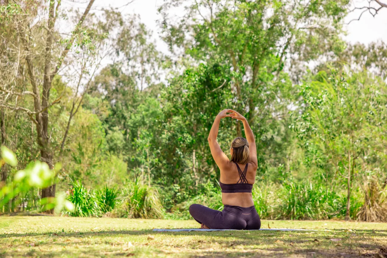 A woman stretching on a yoga mat on a lawn among gum trees