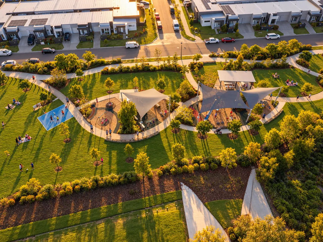 An aerial view of a park with shade sails over two playgrounds, surrounded by homes