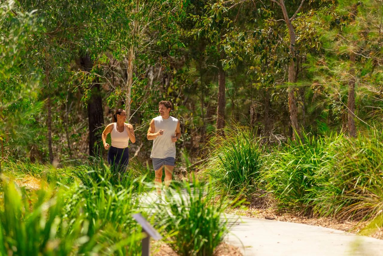 A couple jogging along a bush path through tall grasses and trees