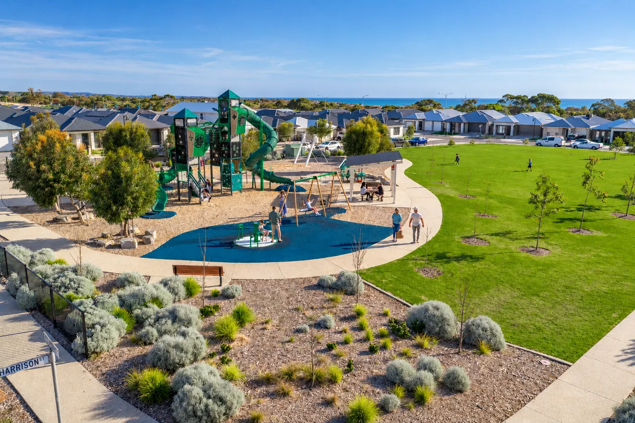 A playground with a tall green play tower and slides beside a lawn and native gardens, with the sea beyond